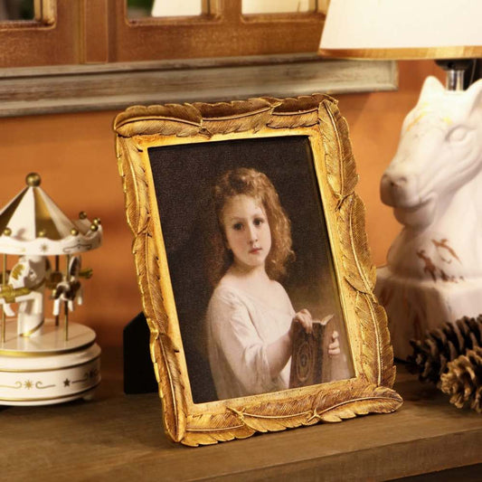 An ornate gold picture frame holding a vintage-style portrait of a young girl, displayed on a wooden shelf next to a white horse figurine, a carousel ornament, and a lamp.