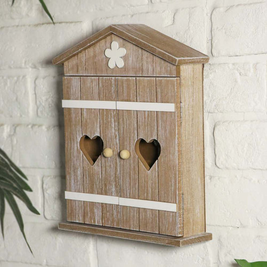 A rustic wooden birdhouse-style wall box with a weathered brown finish, white painted trim, heart-shaped cutouts on the front, and a small white flower detail at the top, mounted against a white brick wall.