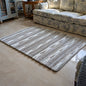 Gray striped rug on a beige floor with a patterned sofa in the background.