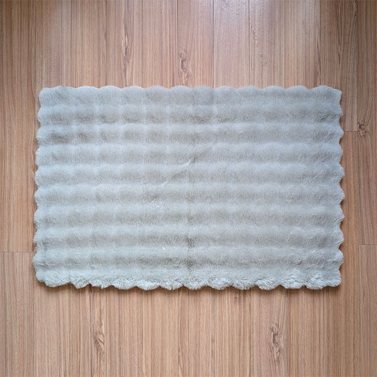 Rectangular white bath mat with scalloped edge on a wooden floor