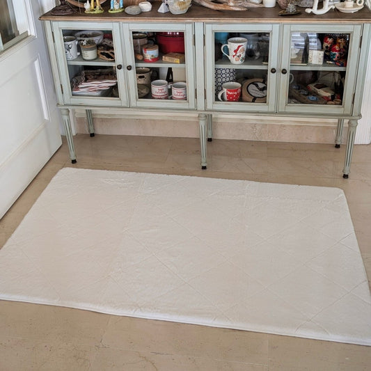 White quilted mat on a marble floor in front of a glass-fronted cabinet.