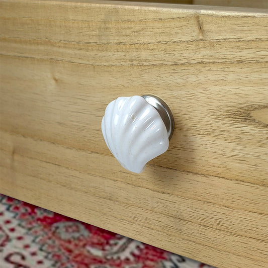 Shell-shaped white cabinet knob on a wooden surface