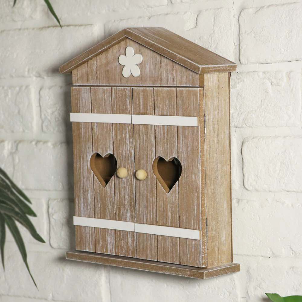 A rustic wooden birdhouse-style wall box with a weathered brown finish, white painted trim, heart-shaped cutouts on the front, and a small white flower detail at the top, mounted against a white brick wall.